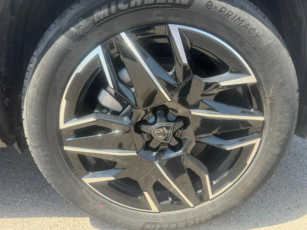 Gros plan sur la jante noire et argentée d’un Peugeot 5008 Hybrid gris, mettant en valeur le logo central et le pneu Michelin.