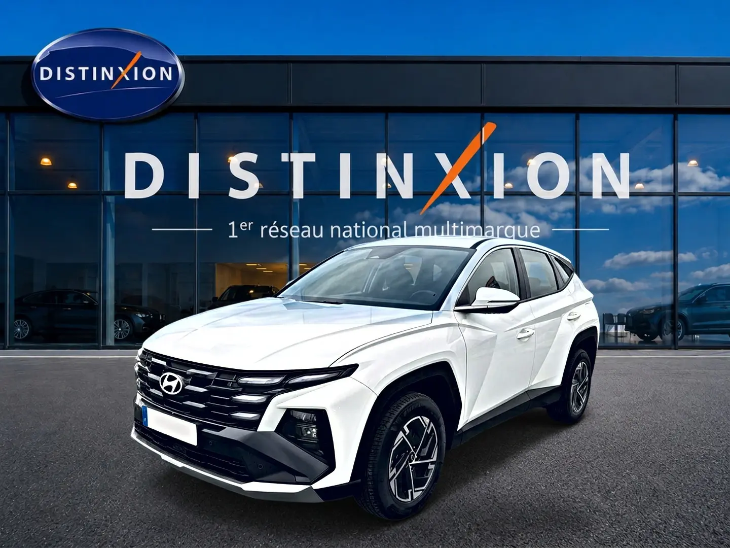 Vue 3/4 avant droite du Hyundai Tucson blanc 2026 avec calandre noire et jantes alliage 17 pouces devant un showroom Distinxion.
