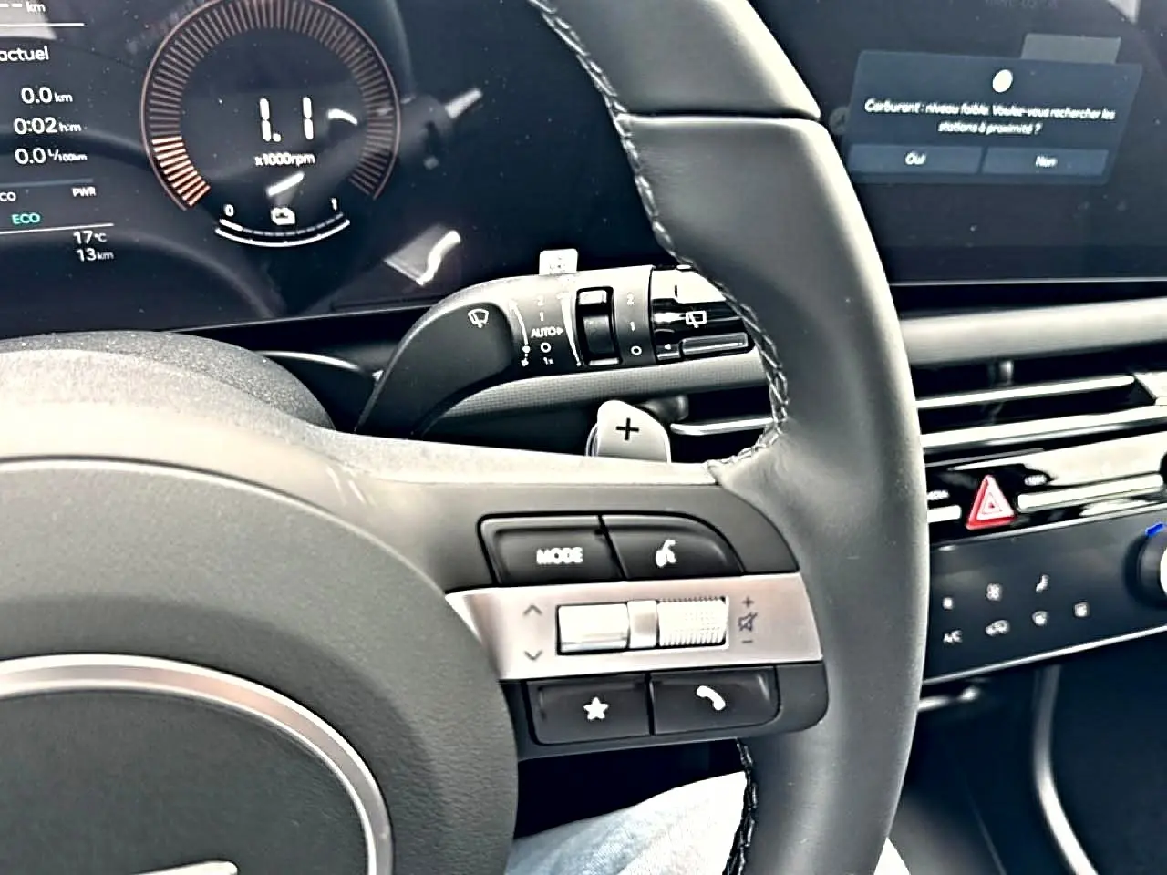Vue rapprochée du volant cuir multifonction noir du Hyundai Tucson blanc, avec commandes audio et écran digital en arrière-plan.