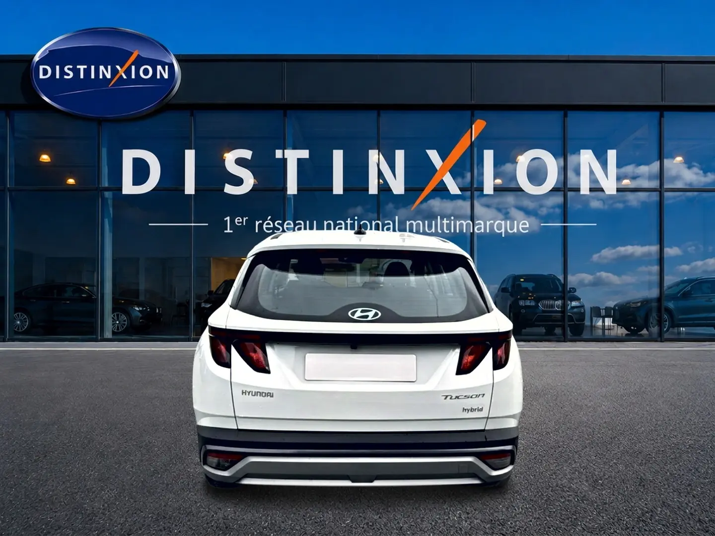 Vue arrière d'un Hyundai Tucson blanc hybride 2026 garé devant une vitrine avec logo Distinxion.