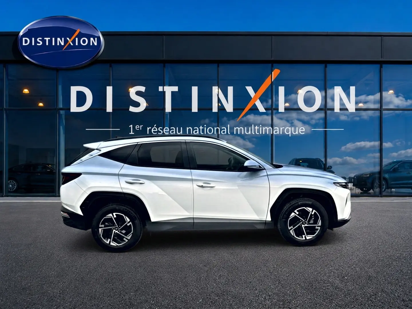 Vue latérale droite d'un Hyundai Tucson blanc 2026 avec jantes alliage 17 pouces devant une vitrine Distinxion.