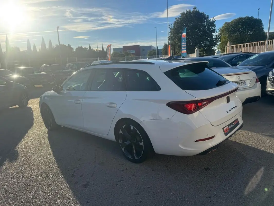 Vue 3/4 arrière droite d'une CUPRA Leon Sportstourer blanche 2024 avec jantes noires et toit ouvrant en extérieur.