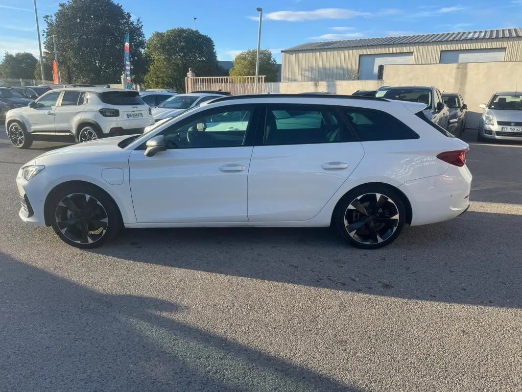 Vue de profil côté gauche d'une CUPRA Leon Sportstourer blanche 2024 avec jantes noires et prise de recharge hybride visible.