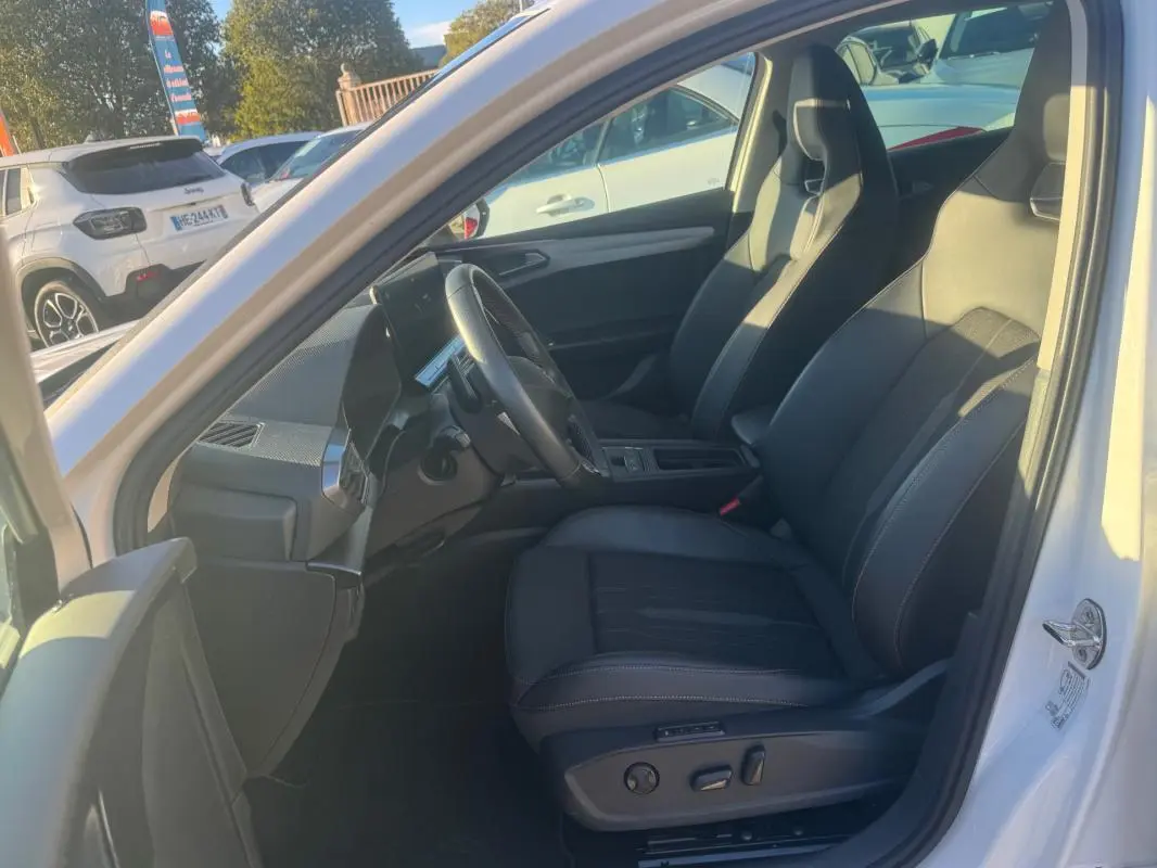 Vue intérieure côté conducteur de la CUPRA Leon Sportstourer blanc 2024, avec sièges sport en cuir noir et tableau de bord moderne.
