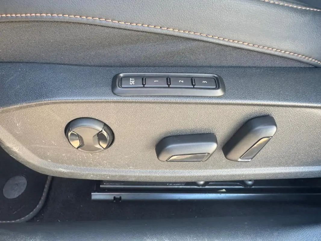 Détail des commandes de réglage électrique des sièges en tissu noir avec surpiqûres contrastantes dans une CUPRA Leon Sportstourer blanche.