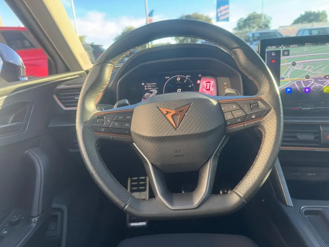 Vue intérieure centrée sur le volant noir perforé avec logo CUPRA cuivré, tableau de bord digital et écran tactile visible.