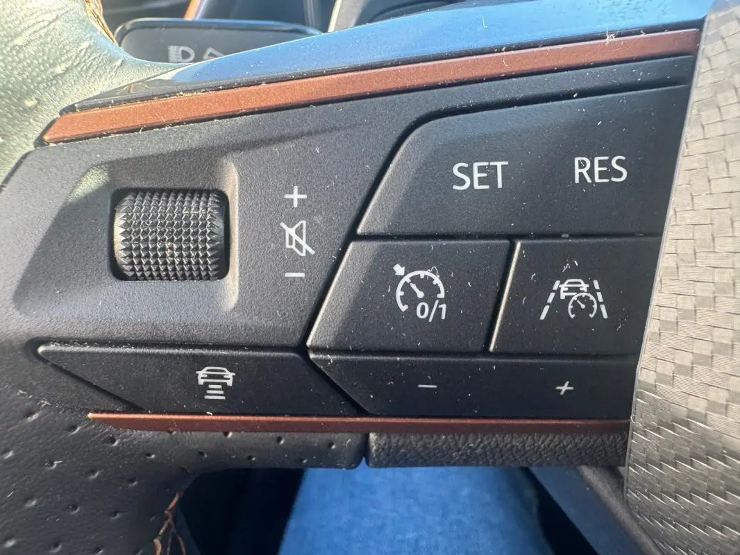 Gros plan sur les commandes noires du volant de la CUPRA Leon Sportstourer blanc, avec boutons de régulateur de vitesse et assistance.