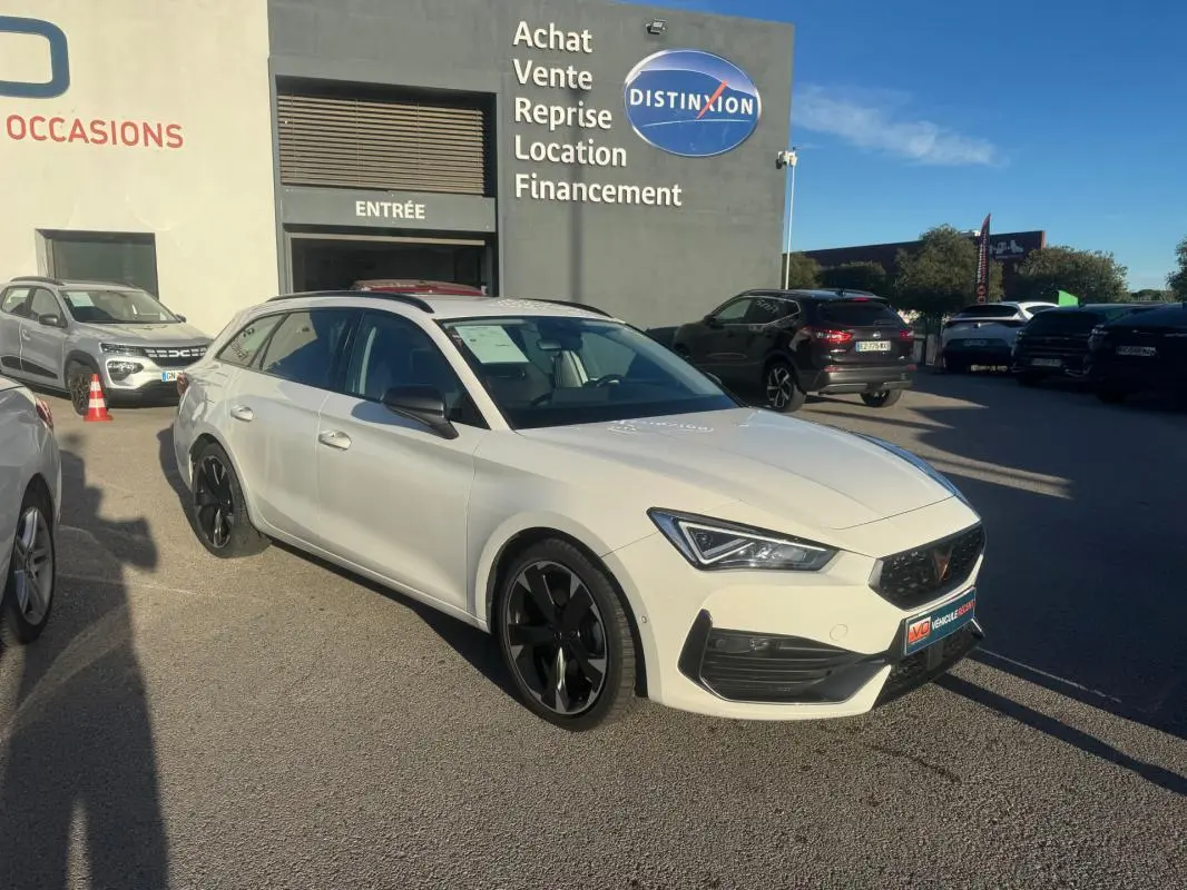 Vue 3/4 avant droite d'une CUPRA Leon Sportstourer blanche 2024 avec jantes noires, devant un concessionnaire.