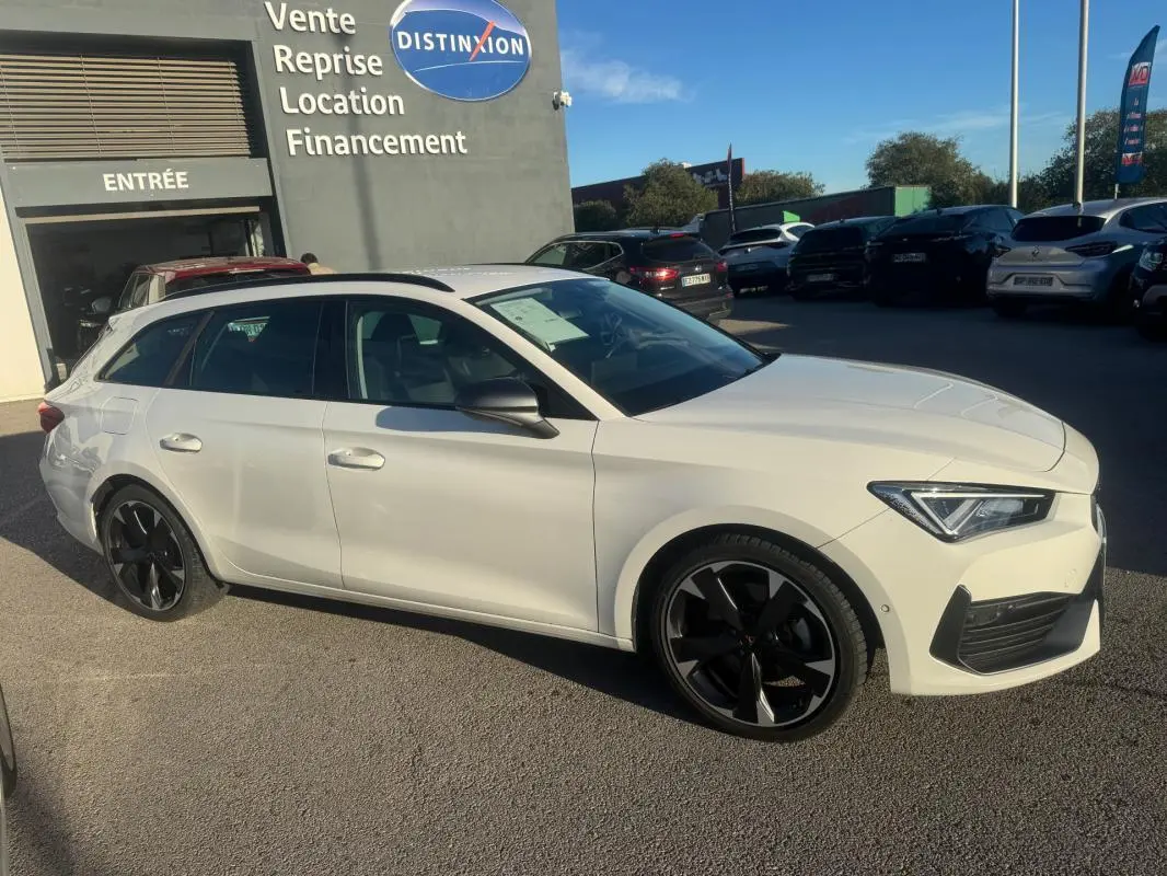 Vue 3/4 avant droite d'une CUPRA Leon Sportstourer blanche 2024 avec jantes noires et toit noir, stationnée en extérieur.