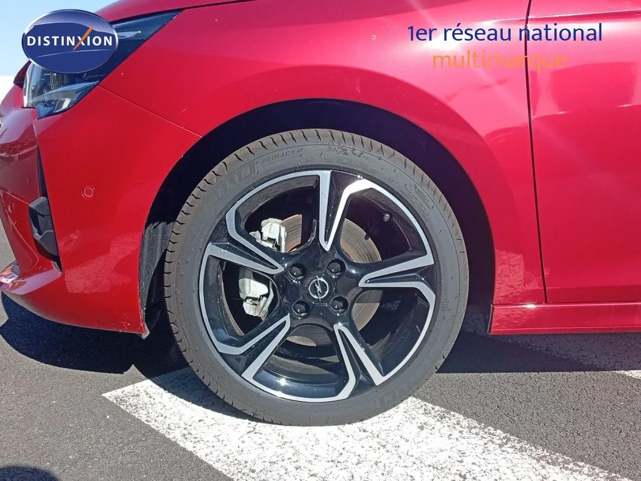 Gros plan sur la roue avant gauche d’une Opel Corsa rouge Kardio métal avec jante noire et détails argentés.