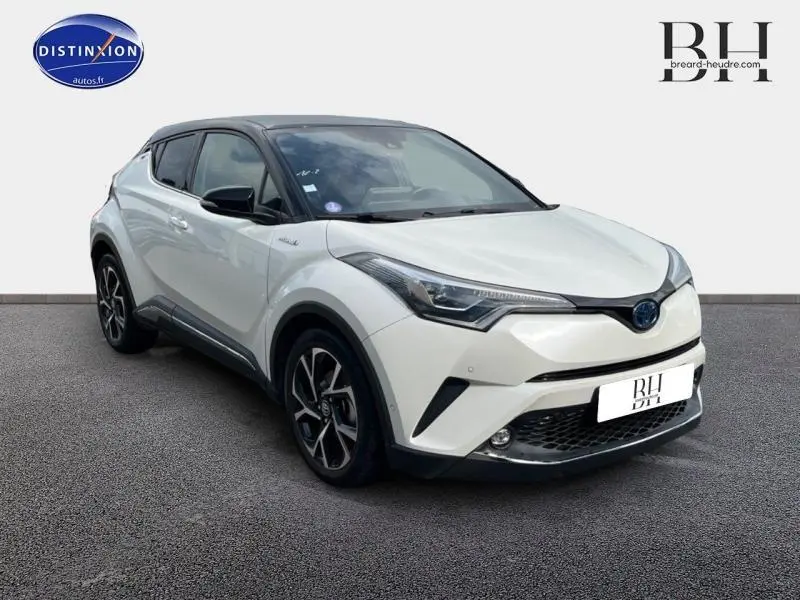 Toyota C-HR 122h Collection blanc nacré bi-ton vu en 3/4 avant droit avec jantes alu et toit noir.