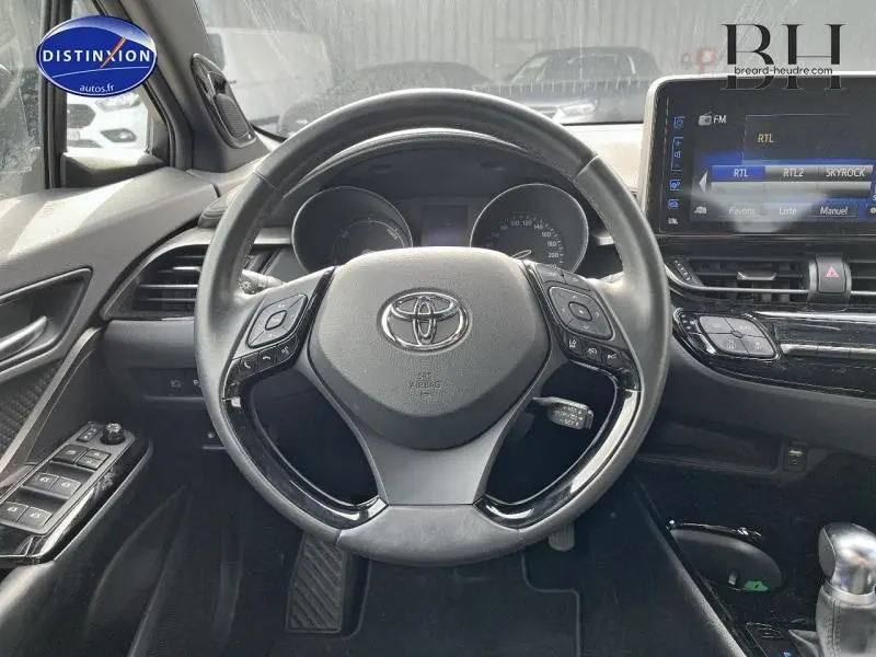 Vue intérieure centrée sur le volant cuir multifonction d'un Toyota C-HR blanc nacré 2019 avec écran tactile et commandes au volant.