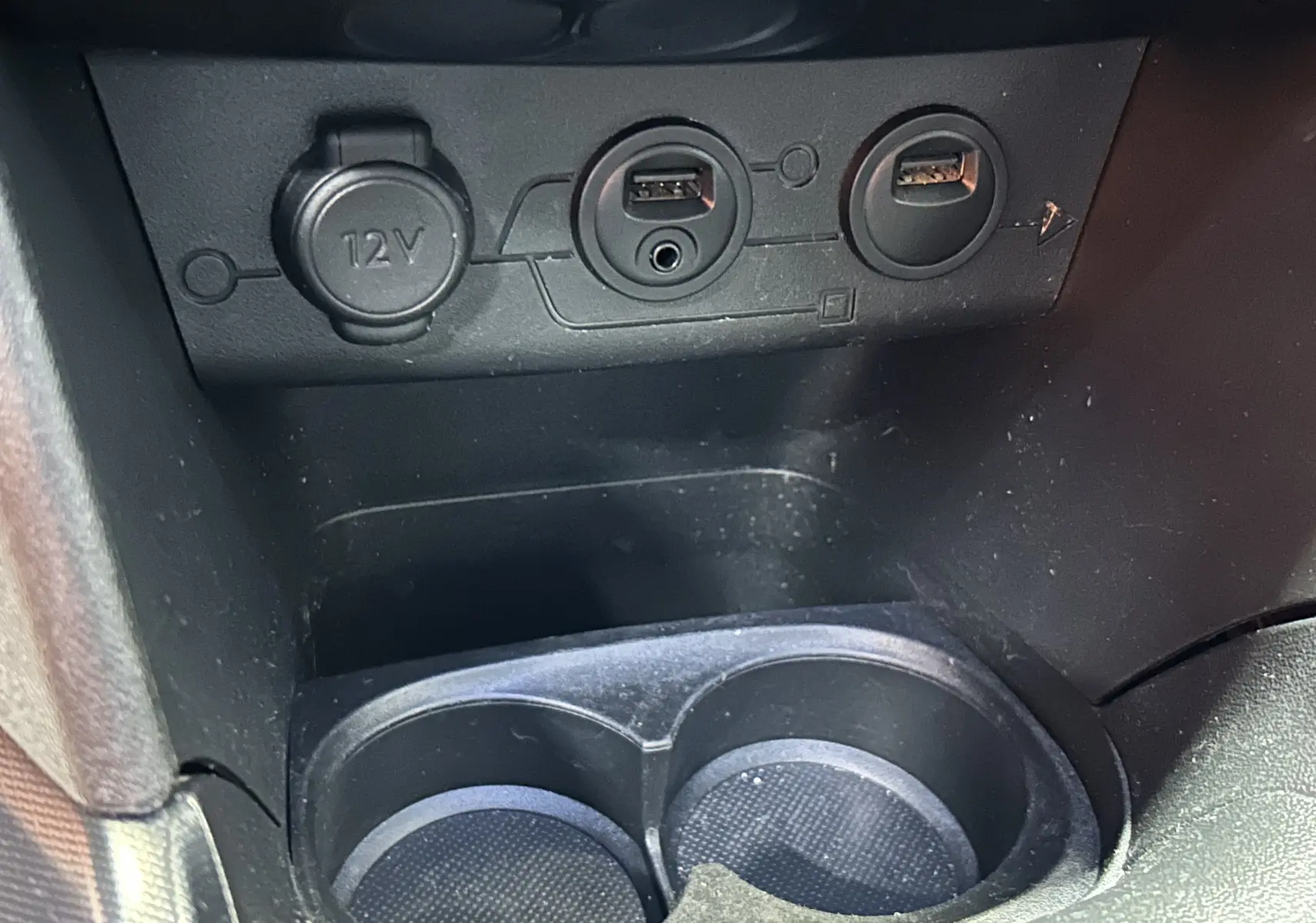 Gros plan sur la console centrale d'une Peugeot 2008 blanche, montrant prises USB, prise 12V et porte-gobelets.