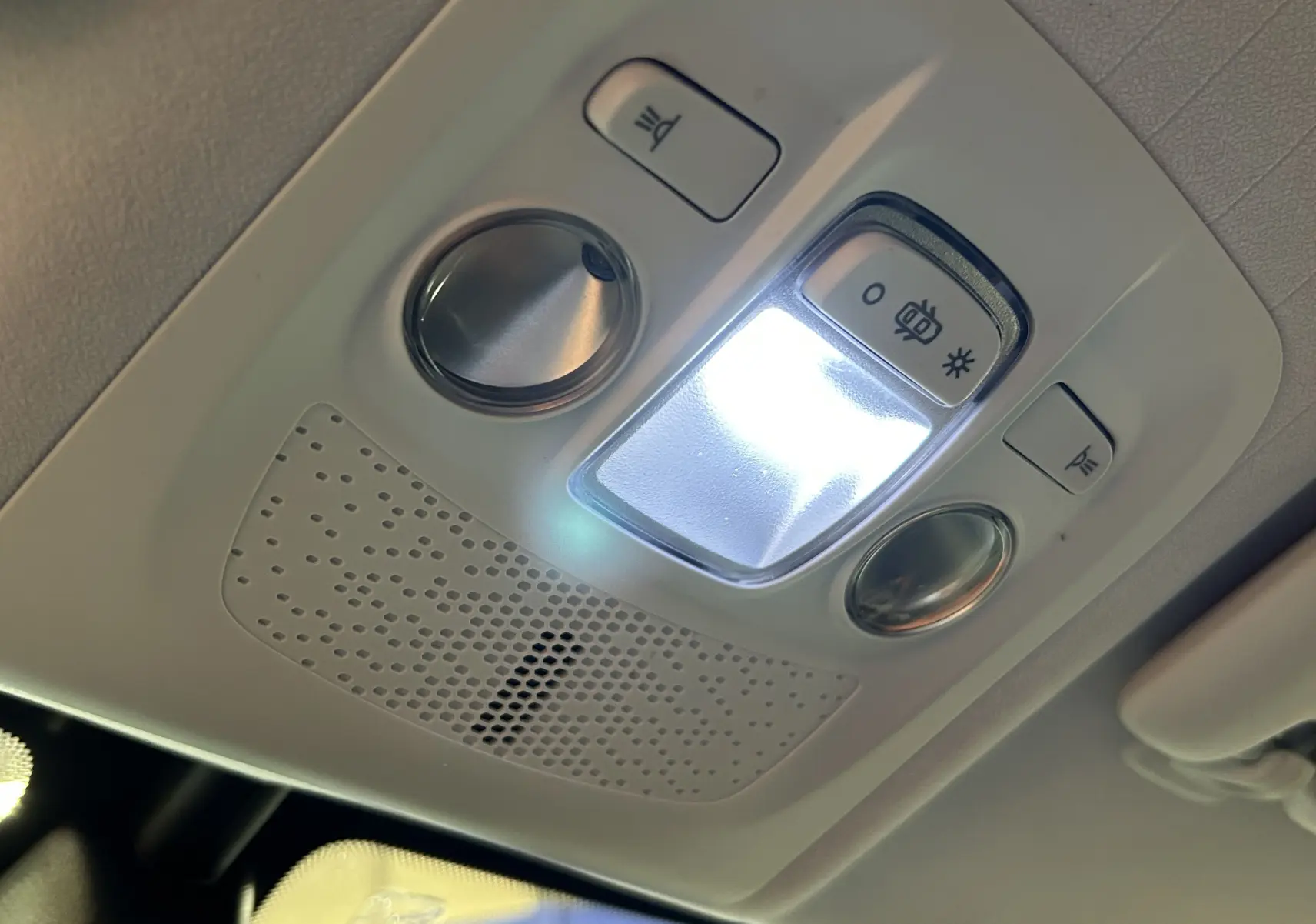 Vue en gros plan du plafonnier intérieur allumé du Peugeot 2008 blanc, avec commandes d’éclairage et haut-parleur intégré.