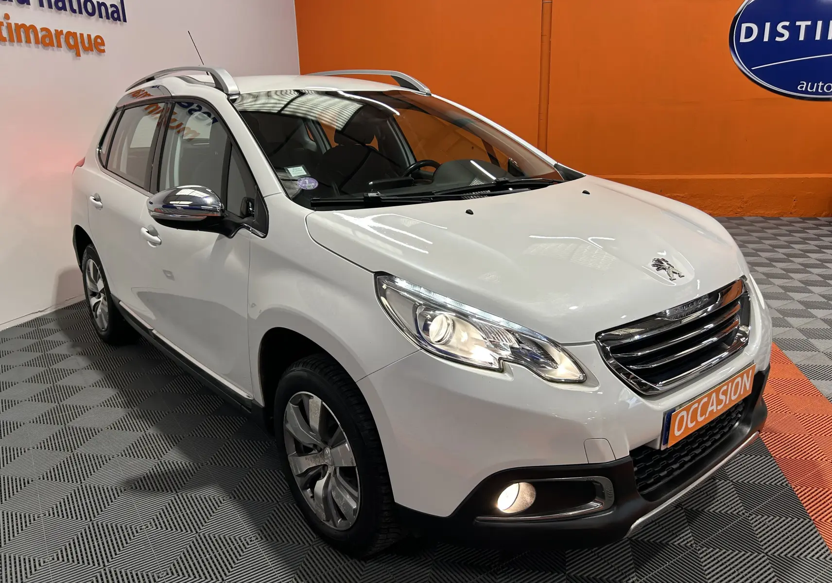 Peugeot 2008 blanc vue 3/4 avant droit avec phares et antibrouillards allumés en intérieur showroom.