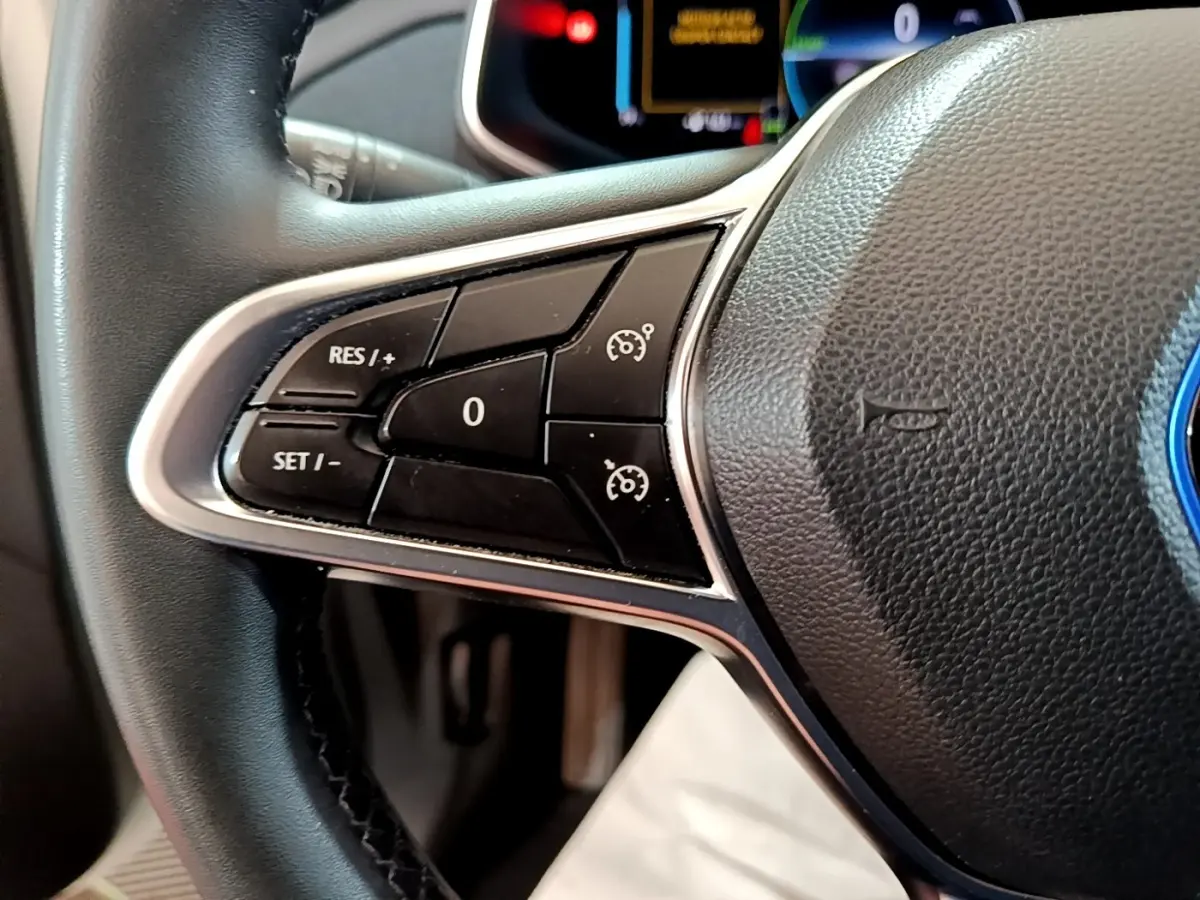 Gros plan sur les commandes du régulateur de vitesse au volant cuir noir de la Renault ZOE Business R110 blanche de 2021.