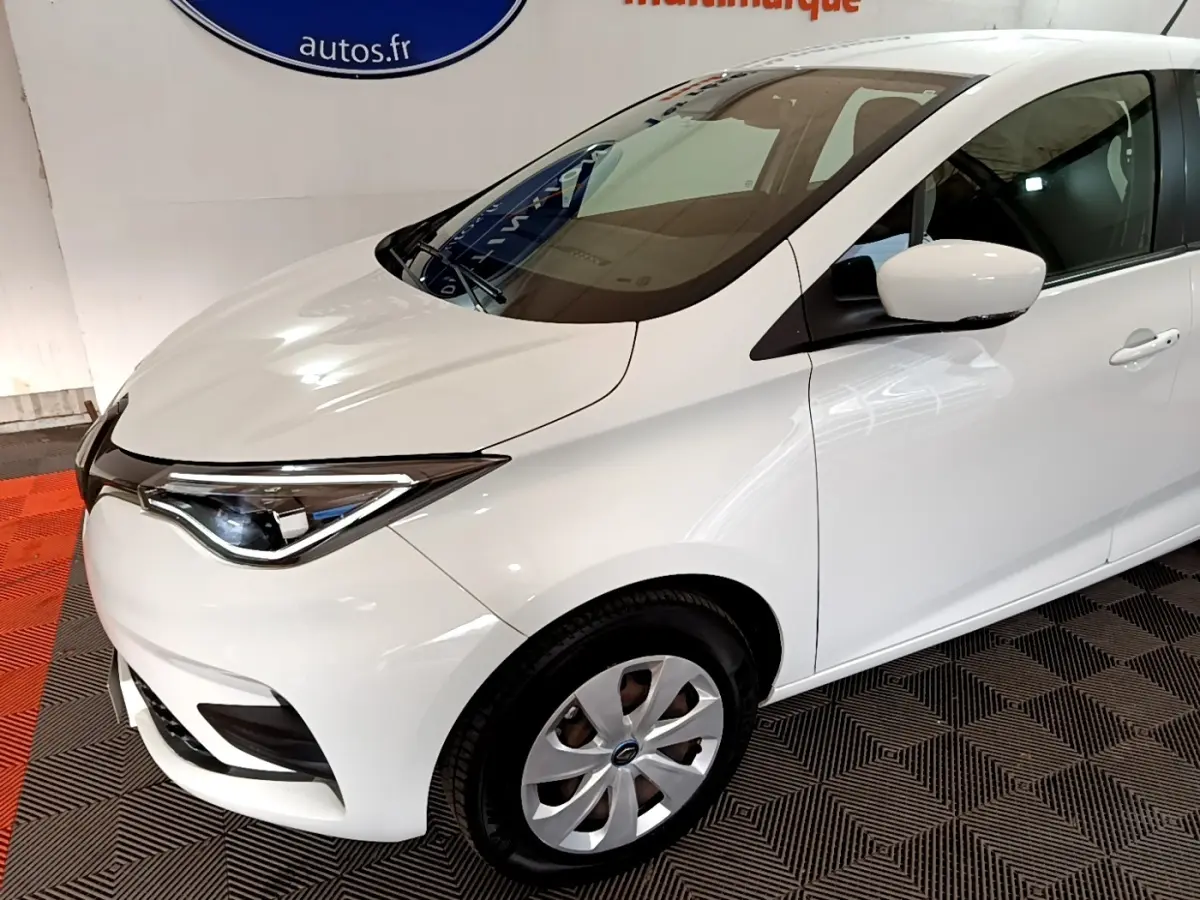 Vue 3/4 avant droit d'une Renault ZOE Business R110 blanche, mettant en valeur ses phares LED et jantes alliage.
