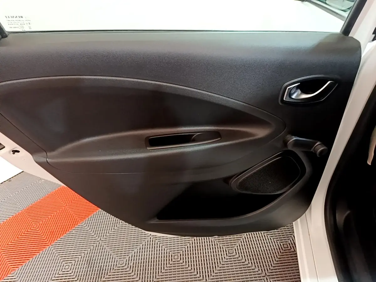 Vue intérieure de la porte avant gauche noire d'une Renault ZOE blanche, avec poignée et haut-parleur intégrés.