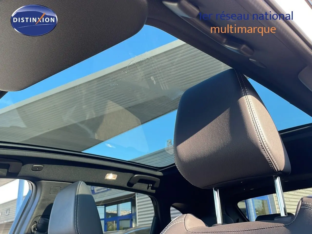 Vue intérieure sur les sièges avant en cuir noir et toit panoramique ouvrant du Nissan Qashqai blanc nacré 2025.