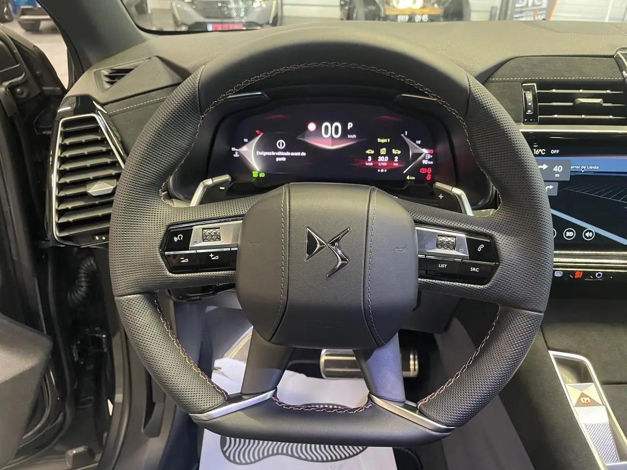 Vue intérieure centrée sur le volant DS en cuir perforé avec surpiqûres Carmin et Or du DS7 Crossback gris titanium.
