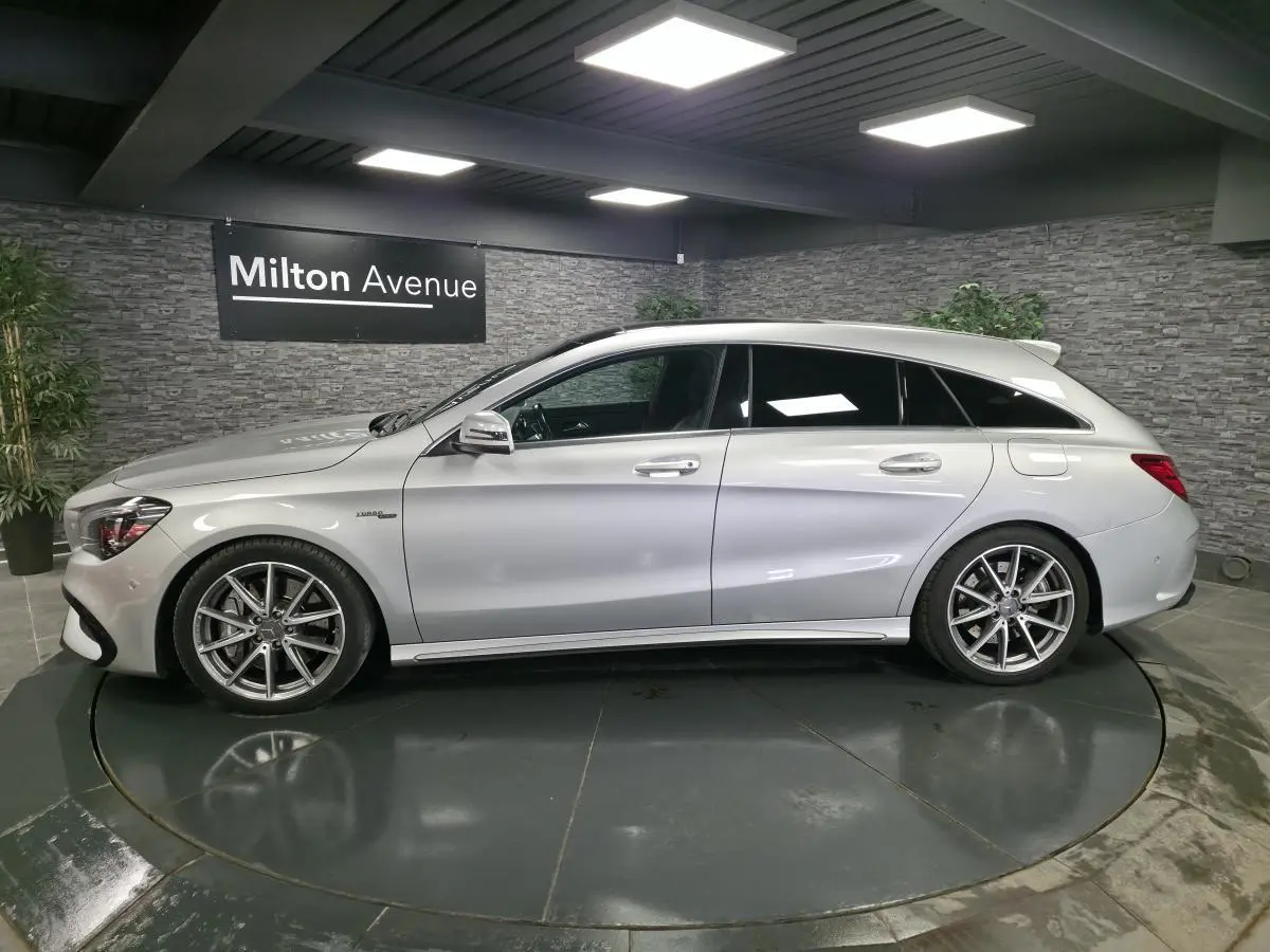 Vue de profil côté gauche d'une Mercedes CLA Shooting Brake 45 AMG gris métallisé en intérieur showroom.
