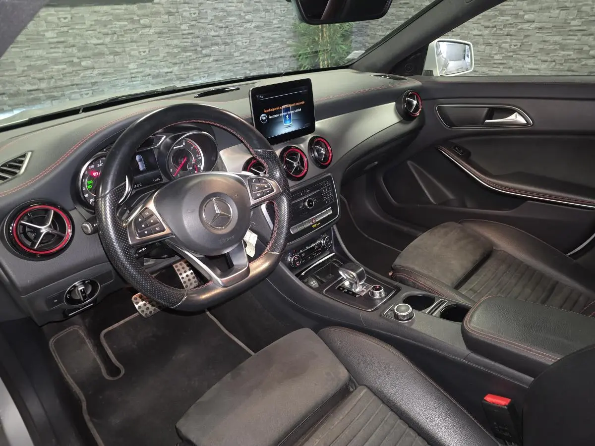 Vue intérieure côté conducteur de la Mercedes CLA Shooting Brake 45 AMG avec volant cuir perforé et finitions rouges.