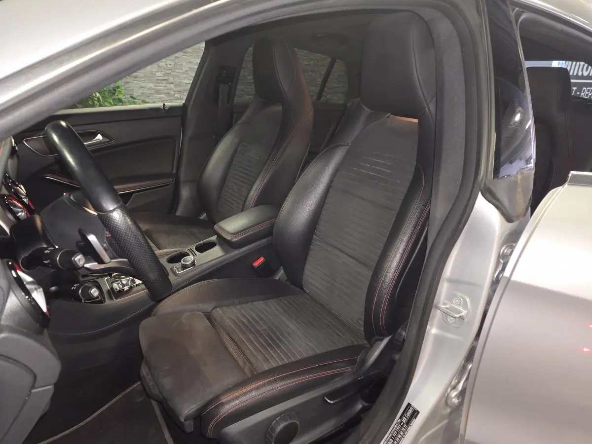 Vue intérieure côté conducteur d'une Mercedes CLA Shooting Brake grise, sièges sport en cuir noir avec surpiqûres rouges.