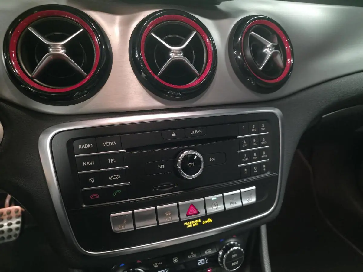 Détail du tableau de bord de la Mercedes CLA Shooting Brake 45 AMG 2016 avec aérateurs ronds à contour rouge et console centrale noire.
