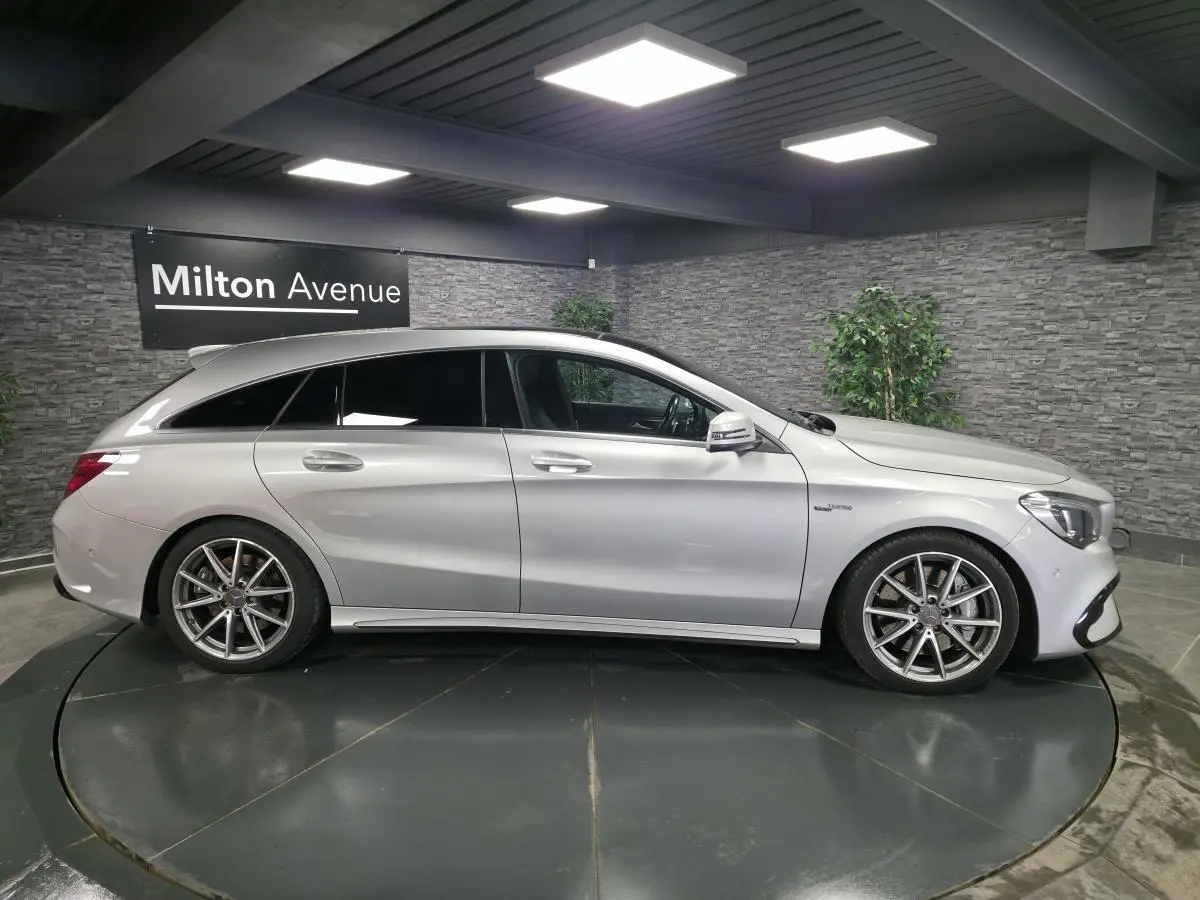 Vue de profil côté gauche d'une Mercedes Classe CLA Shooting Brake gris métallisé avec jantes AMG 18 pouces en intérieur showroom.
