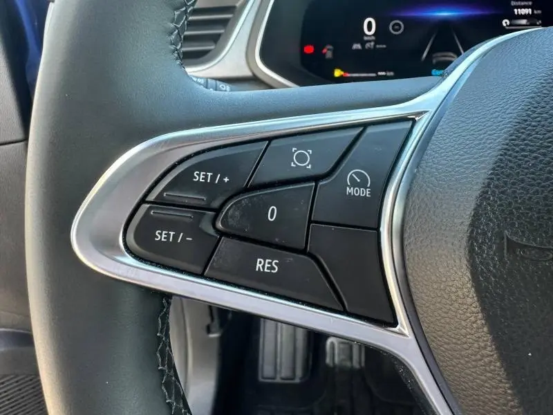 Gros plan sur les commandes au volant côté gauche du Renault Captur 2025 Bleu Iron/Noir Etoilé, avec tableau de bord numérique en arrière-plan.