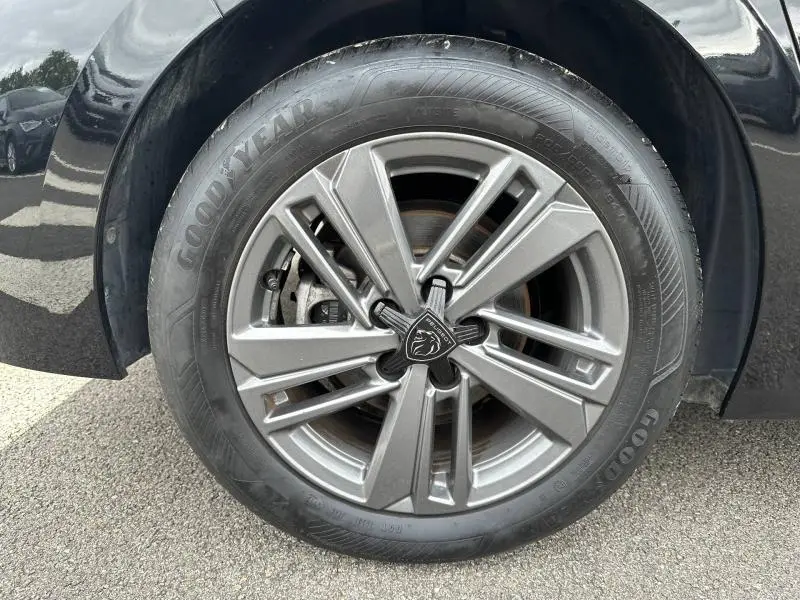Gros plan sur la roue avant gauche d'une Peugeot 308 2024 noire Perla Nera avec jante alliage et logo lion central.