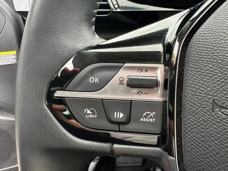 Gros plan sur les commandes au volant côté gauche de la Peugeot 308 2024 en Noir Perla Nera, avec boutons de régulateur et assistances.