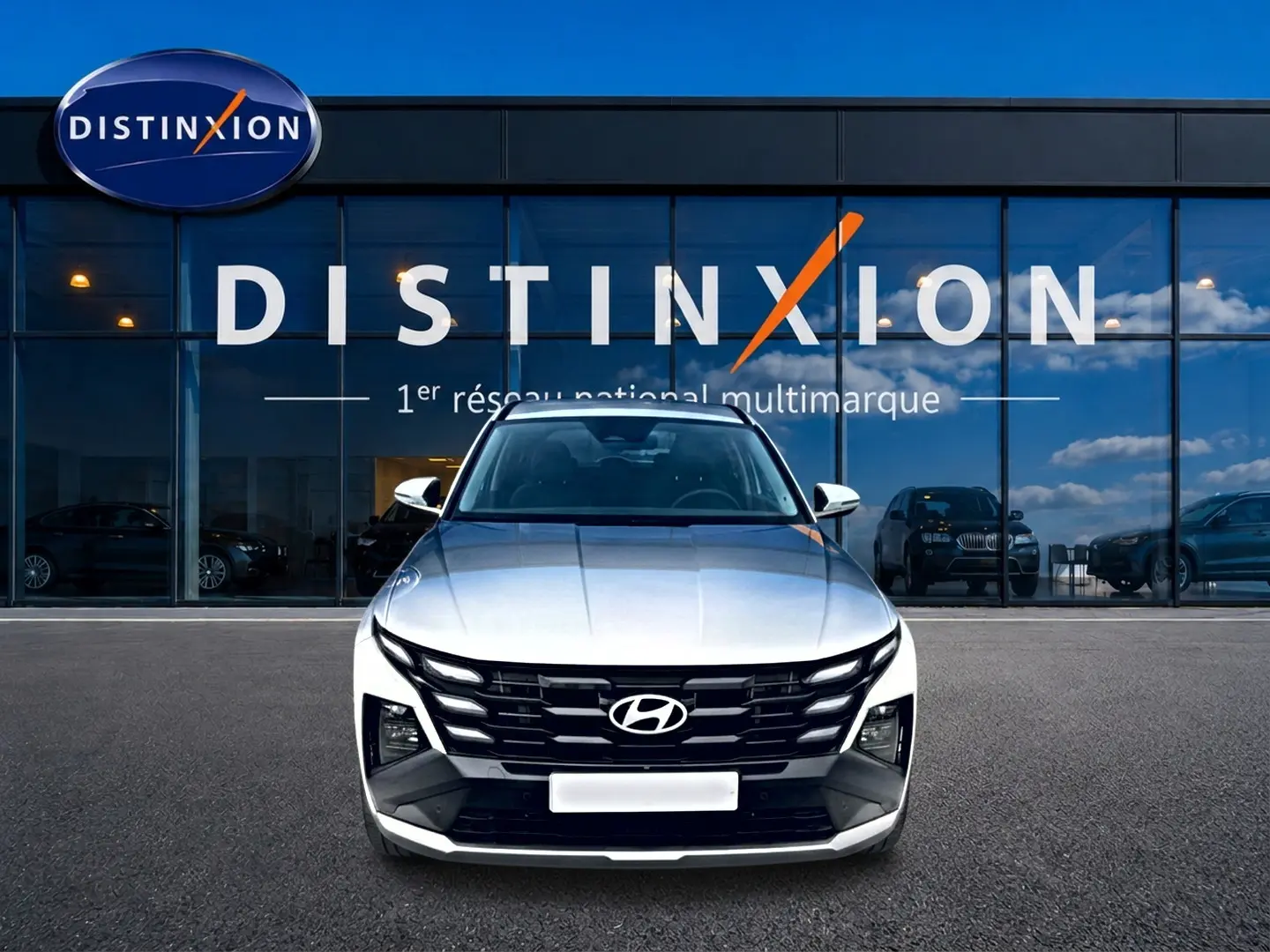 Vue avant d'un Hyundai Tucson blanc 2026 avec calandre noire et logo Hyundai, devant une vitrine Distinxion.