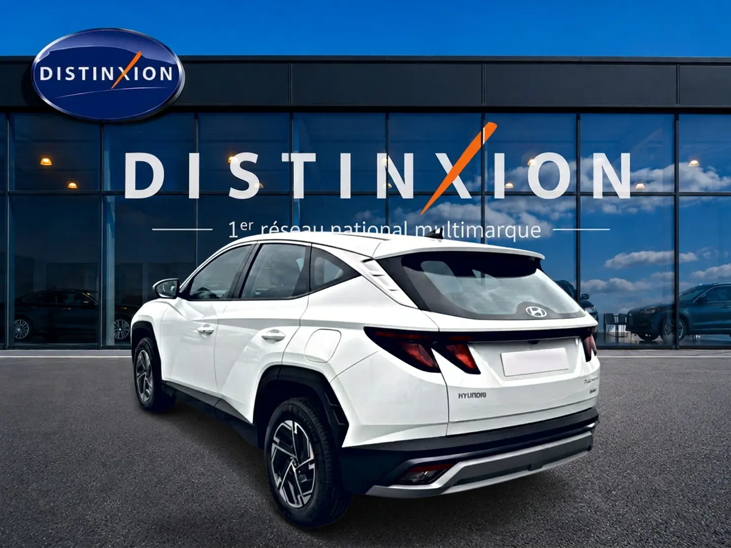 Vue 3/4 arrière droite d'un Hyundai Tucson blanc 2026 hybride devant une vitrine Distinxion.