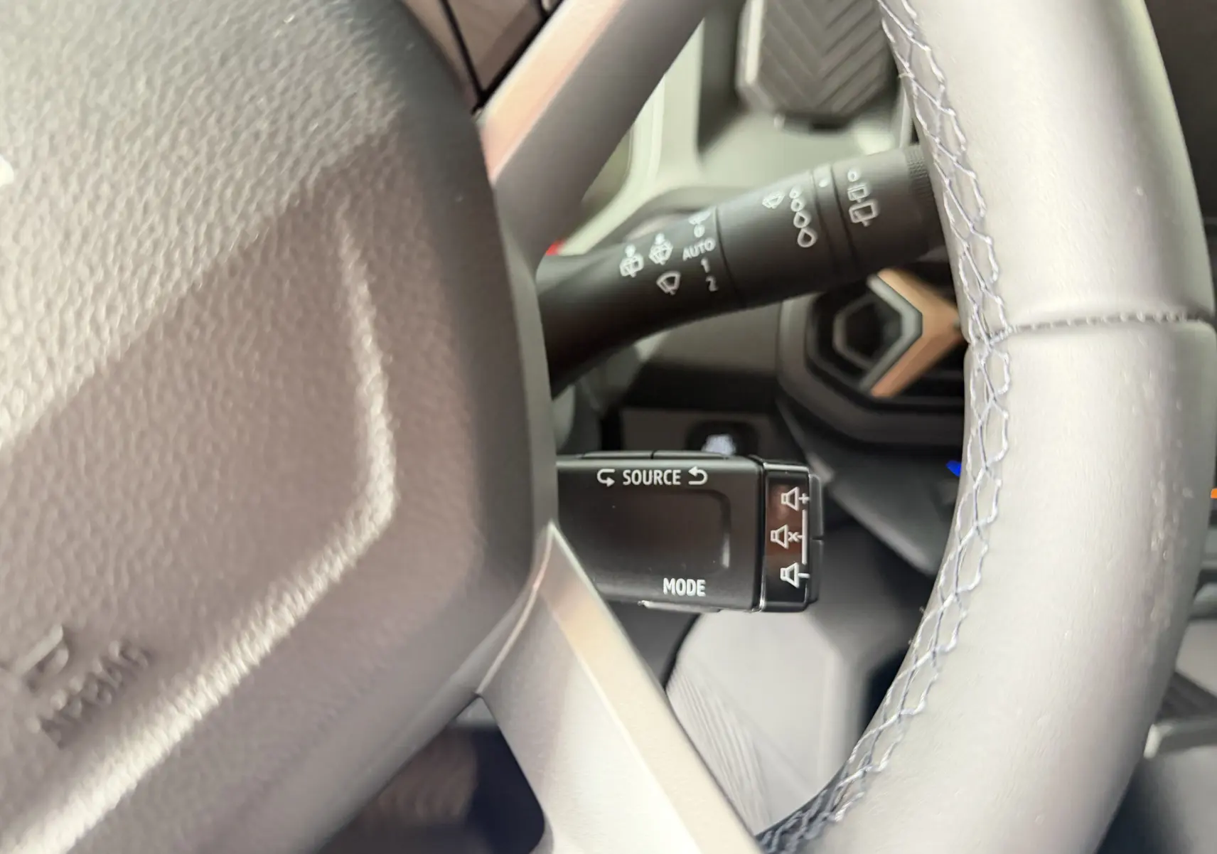Gros plan sur la commande multimédia au volant du Dacia Duster Hybrid 155 Extreme, intérieur gris avec coutures bleues.