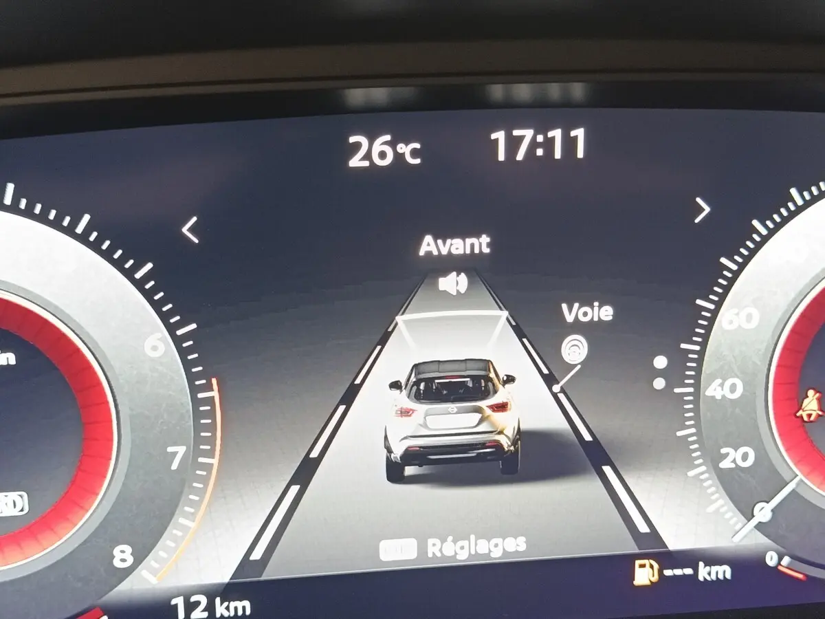 Affichage numérique du tableau de bord montrant une voiture blanche vue de dos sur une route virtuelle, température 26°C, heure 17:11.