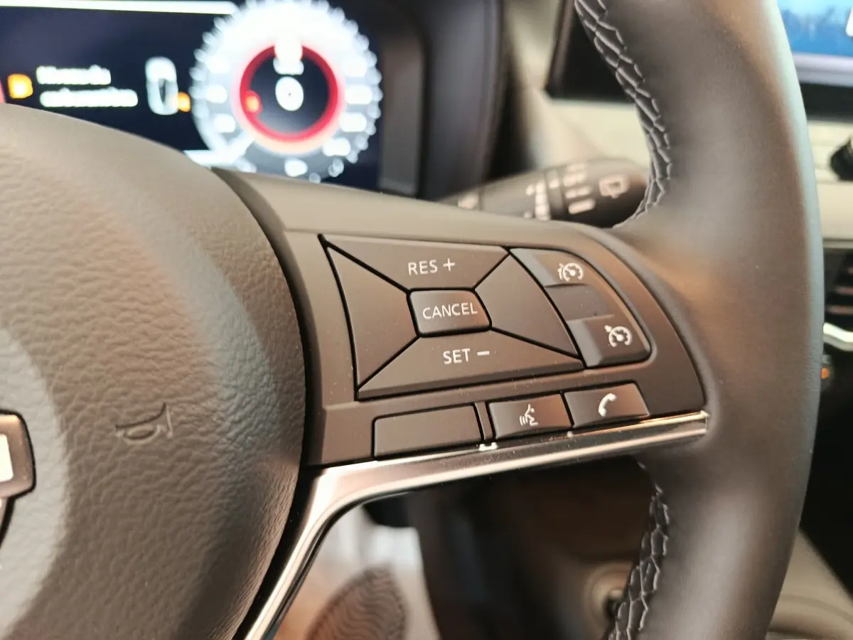 Gros plan sur les commandes du régulateur de vitesse au volant cuir noir du Nissan Juke DIG-T 114 BVM6 N-Connecta 2025.