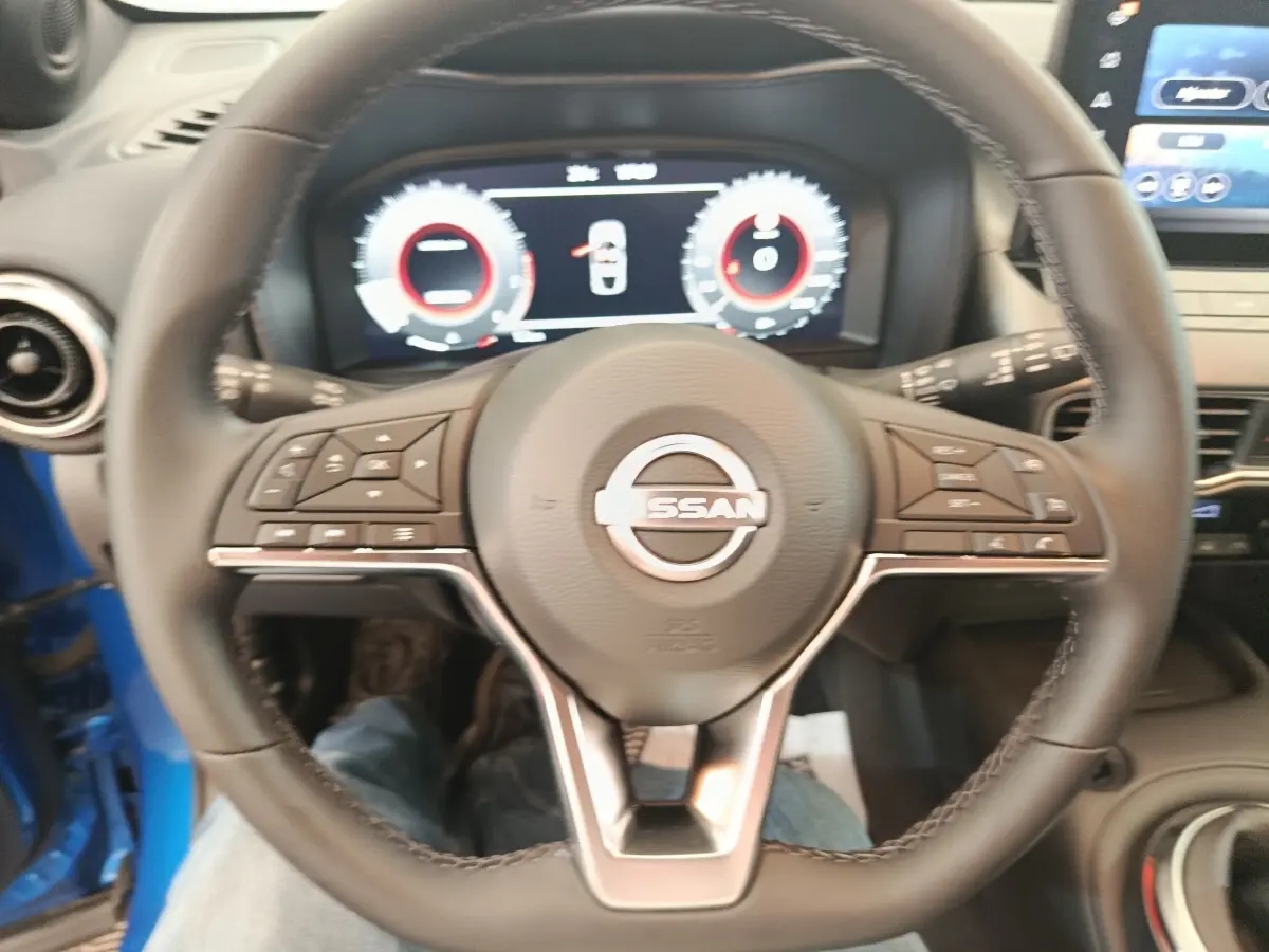 Vue intérieure centrée sur le volant cuir du Nissan Juke bleu 2025 avec tableau de bord numérique et écran tactile.