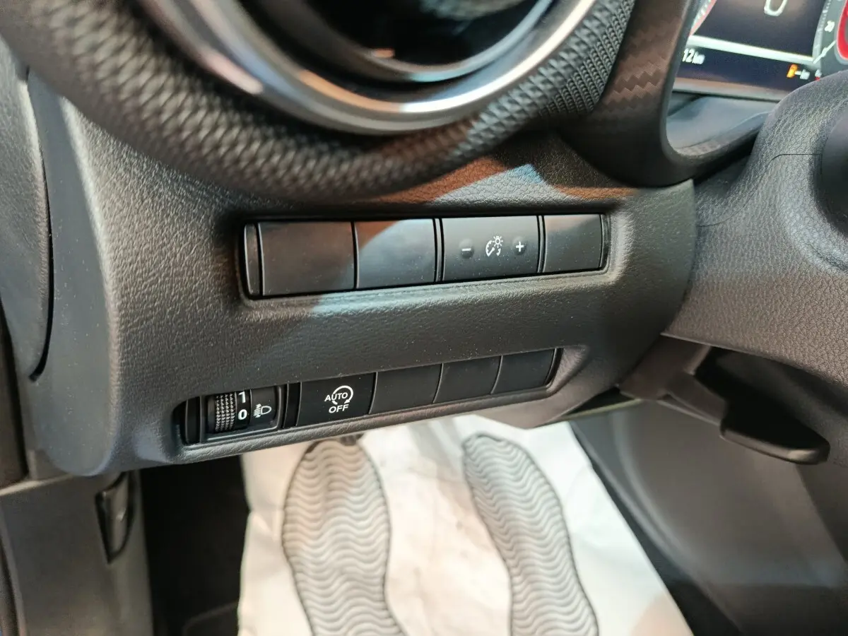 Gros plan sur les commandes d’éclairage et réglage du tableau de bord côté gauche dans l’habitacle noir du Nissan Juke bleu 2025.