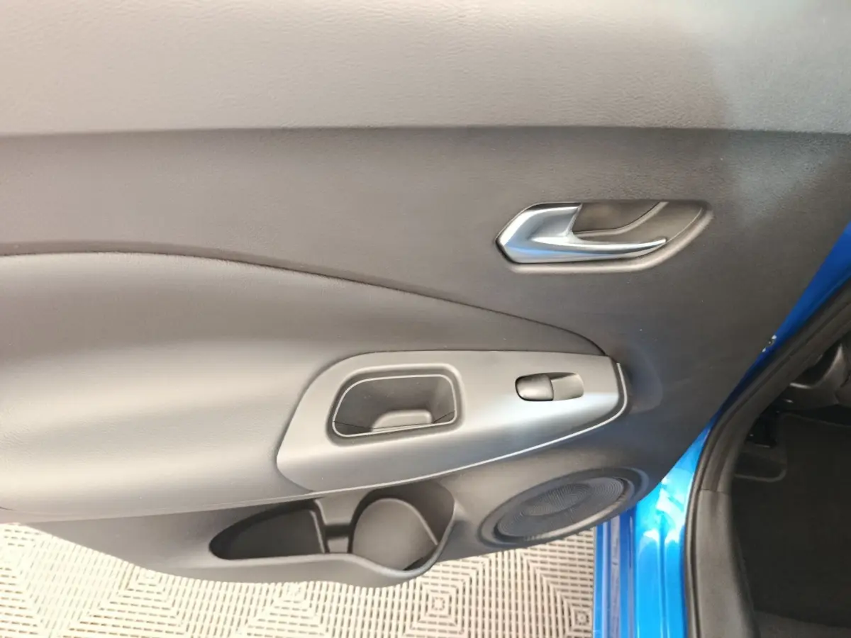 Intérieur côté gauche de la porte avant d’un Nissan Juke bleu 2025, avec poignée argentée et haut-parleur intégré.