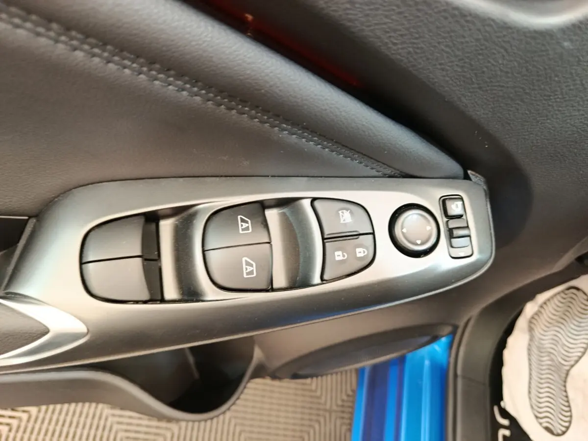 Gros plan sur les commandes de lève-vitres et rétroviseurs côté conducteur du Nissan Juke bleu 2025.