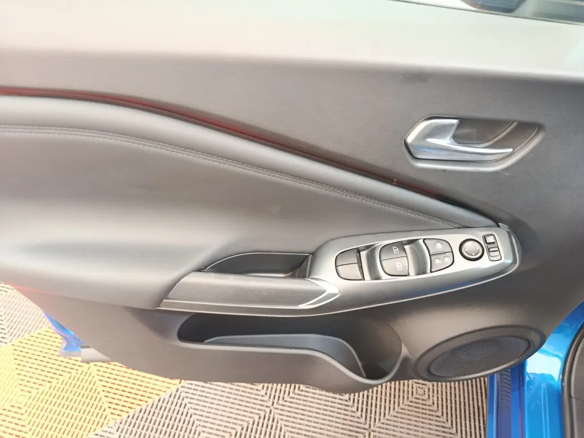 Intérieur de la porte avant gauche du Nissan Juke bleu, avec commandes de vitres et poignée argentée.