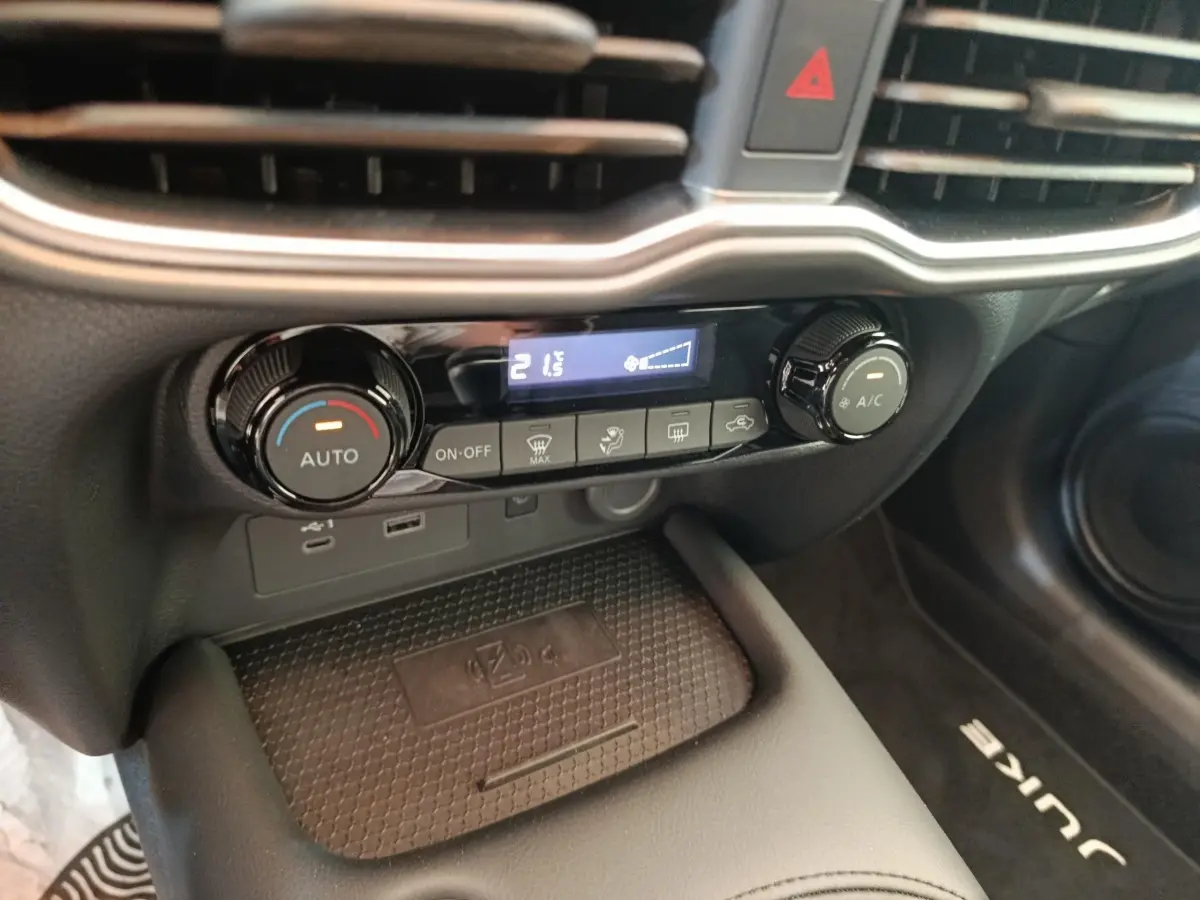 Gros plan sur la console centrale du Nissan Juke 2025, montrant les commandes de climatisation et la zone de recharge sans fil.