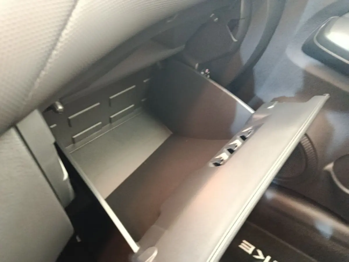 Vue rapprochée de la boîte à gants ouverte côté passager du Nissan Juke bleu 2025, intérieur noir.