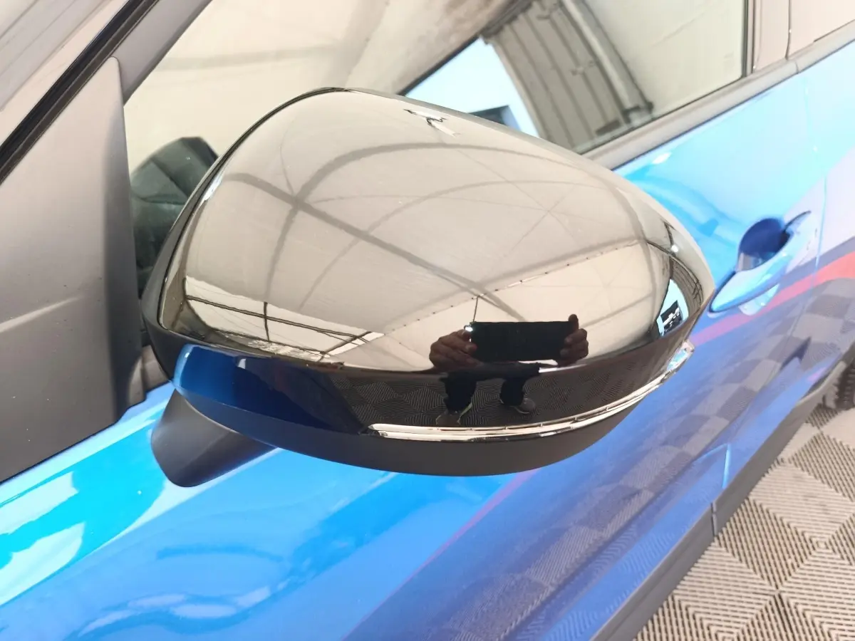 Rétroviseur droit noir brillant sur Nissan Juke bleu, vue rapprochée côté conducteur avec poignée de porte visible.