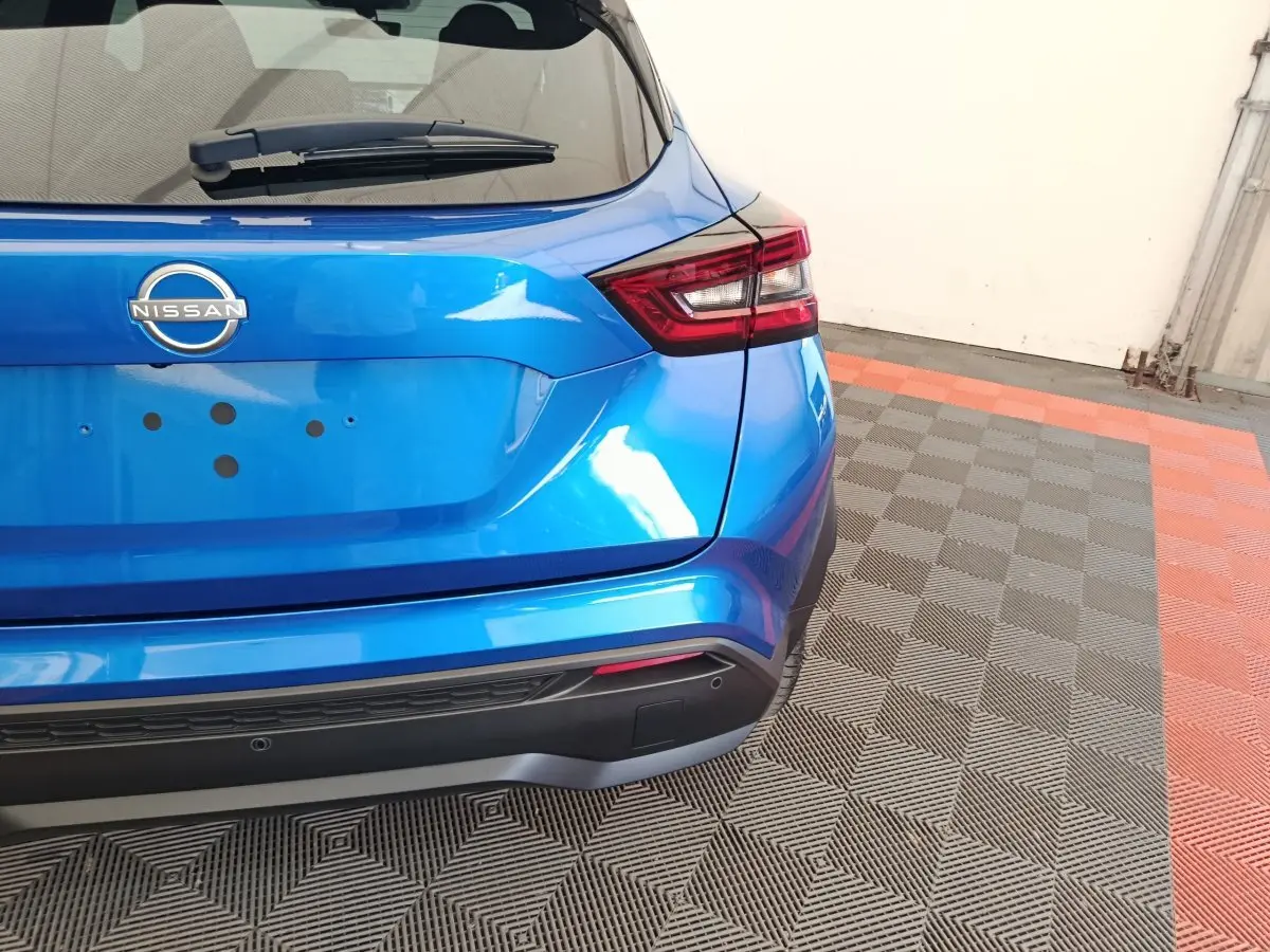 Vue arrière droite d'un Nissan Juke bleu 2025 avec feux LED et pare-chocs noir mat sur sol carrelé.