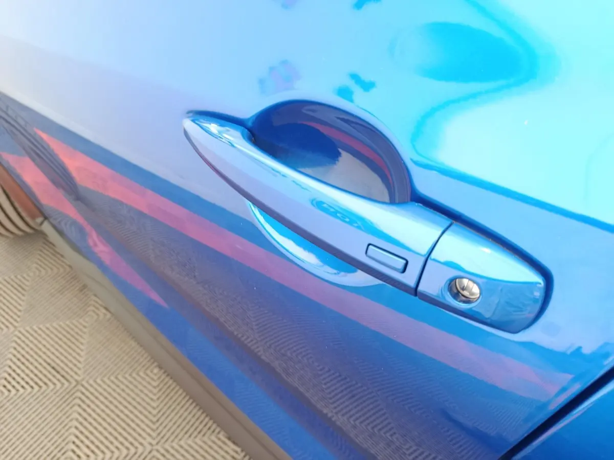Poignée de porte côté droit bleu vif d'une Nissan Juke 2025 DIG-T 114 BVM6 N-Connecta en gros plan.