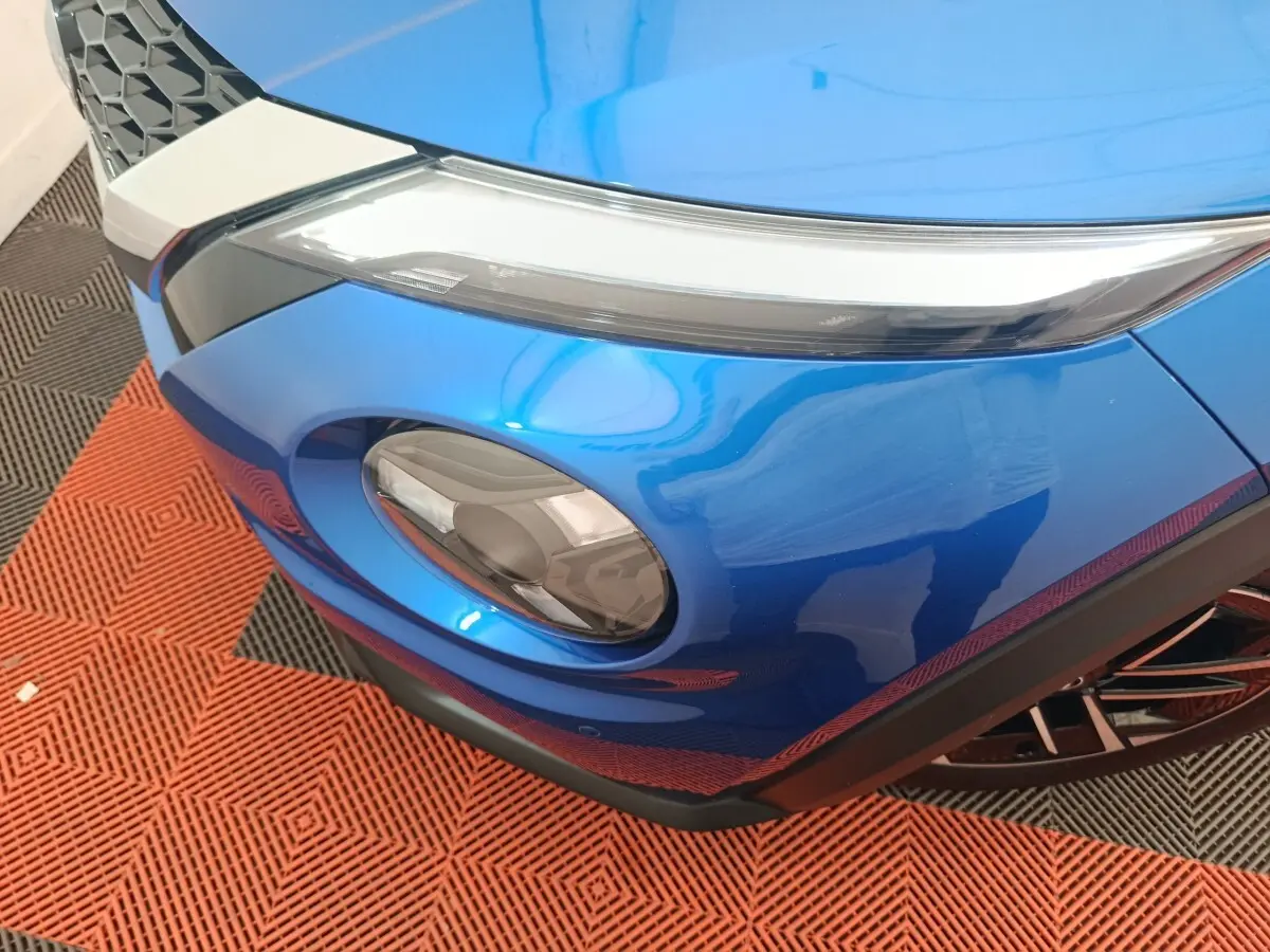 Gros plan sur le phare avant droit bleu vif du Nissan Juke 2025 avec détails du pare-chocs noir et calandre.