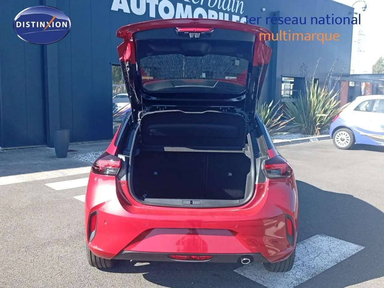 Vue arrière d’une Opel Corsa rouge Kardio métal avec toit noir, coffre ouvert montrant l’espace de chargement.