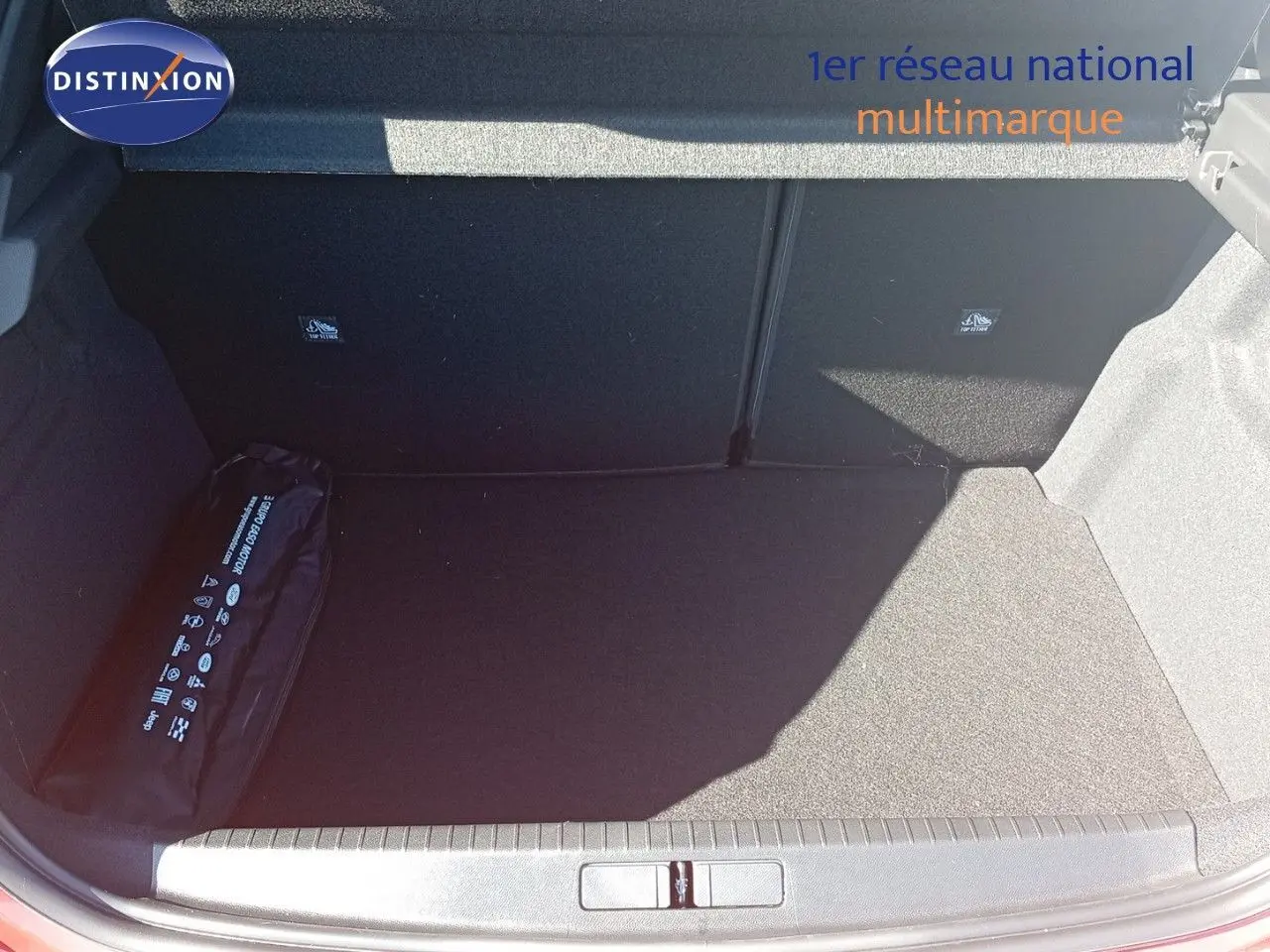 Coffre ouvert d’une Opel Corsa rouge Kardio métal avec toit noir, montrant un espace de chargement vide et un kit de sécurité.